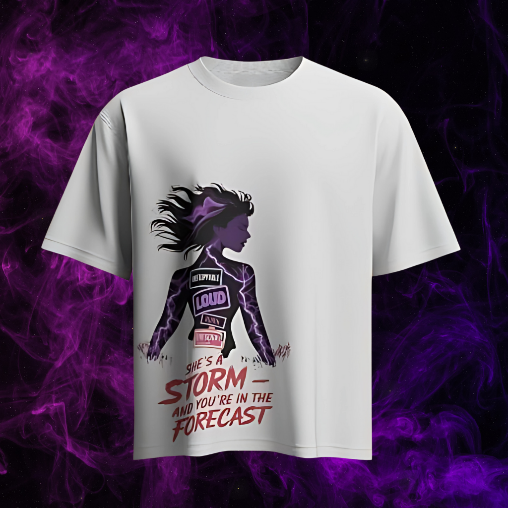 White t-shirt with a graphic of a woman emitting purple lightning and the text "SHE'S A STORM - AND YOU'RE IN THE FORECAST."